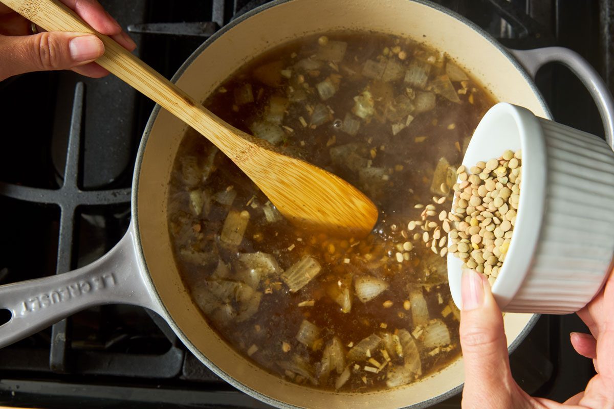 overhead photo of onions and lentils being cooked in pot on stove
