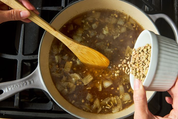 overhead photo of onions and lentils being cooked in pot on stove