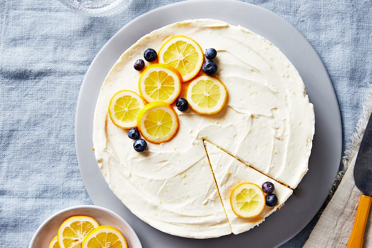 No Bake Lemon Cheesecake Hero- whole cake decorated with lemon slices and berries, one piece sliced