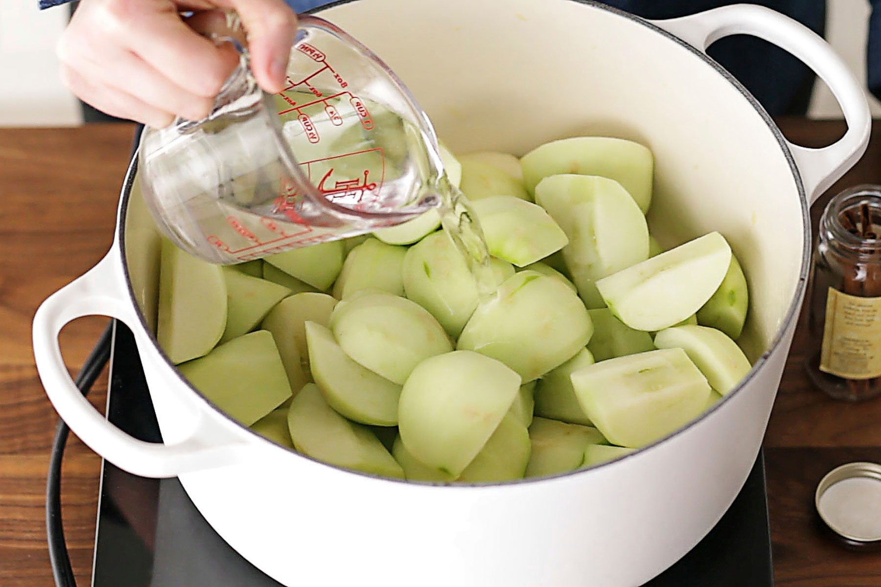 Person pouring water over peeled apples in a dutch oven