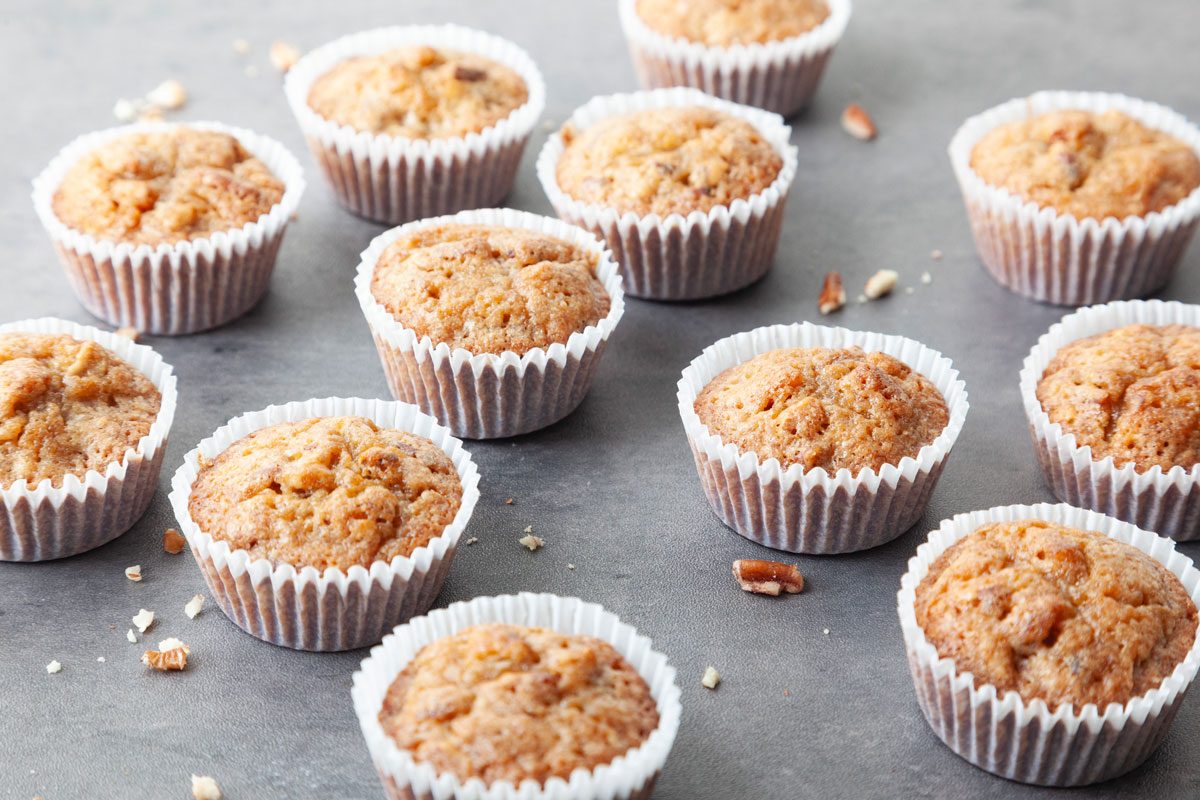 Full yield of Taste of Home Pecan Pie Muffins on a black surface, scattered with pecan pieces