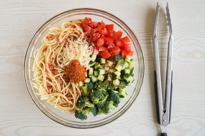 Tossing together pasta salad with broccoli, tomatoes, and cucumber
