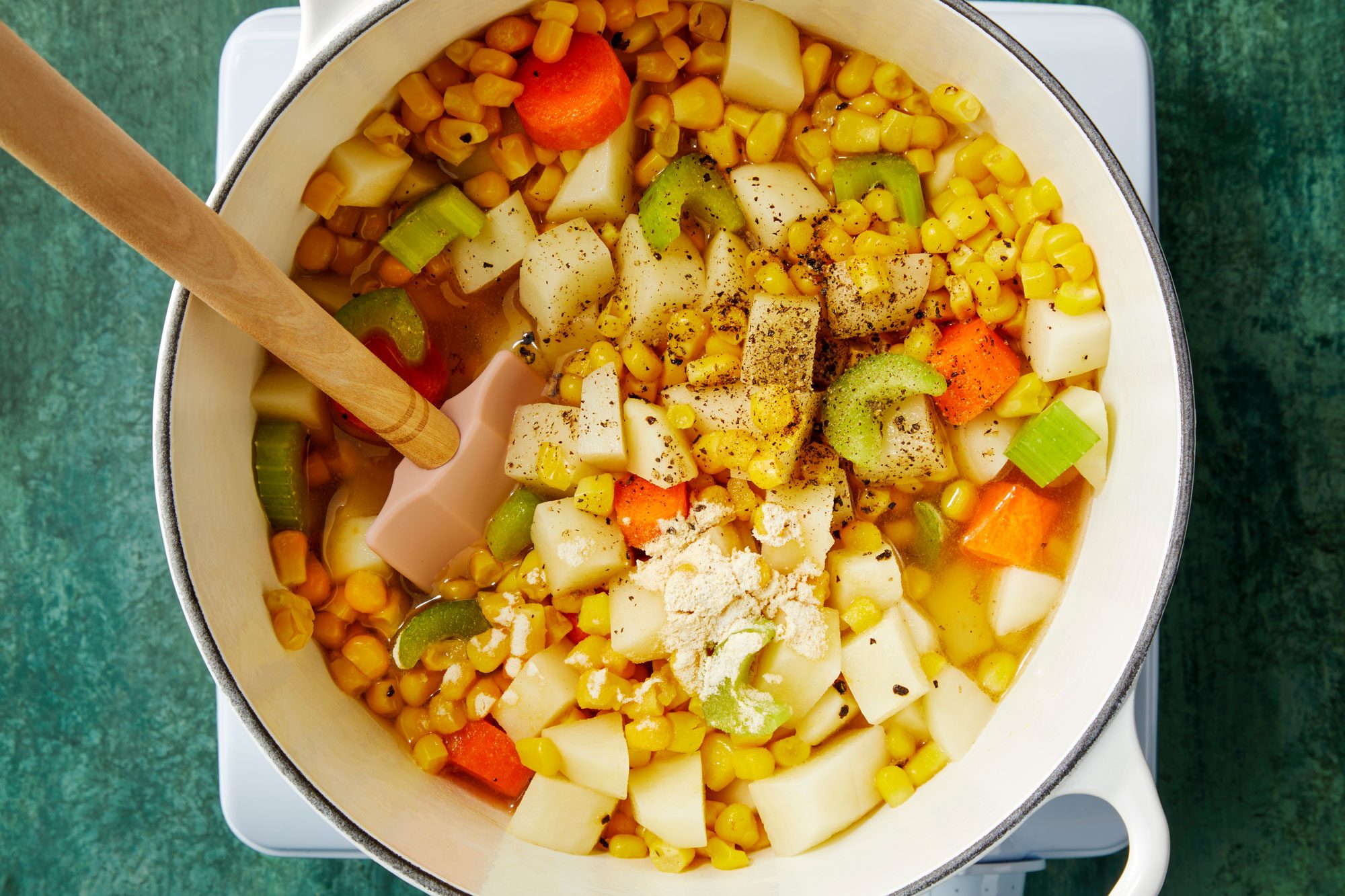 Overhead shot of the same pan; combine the potatoes; corn; broth; celery; carrot and seasonings; bring to a boil; induction; spatula; green texture surface;