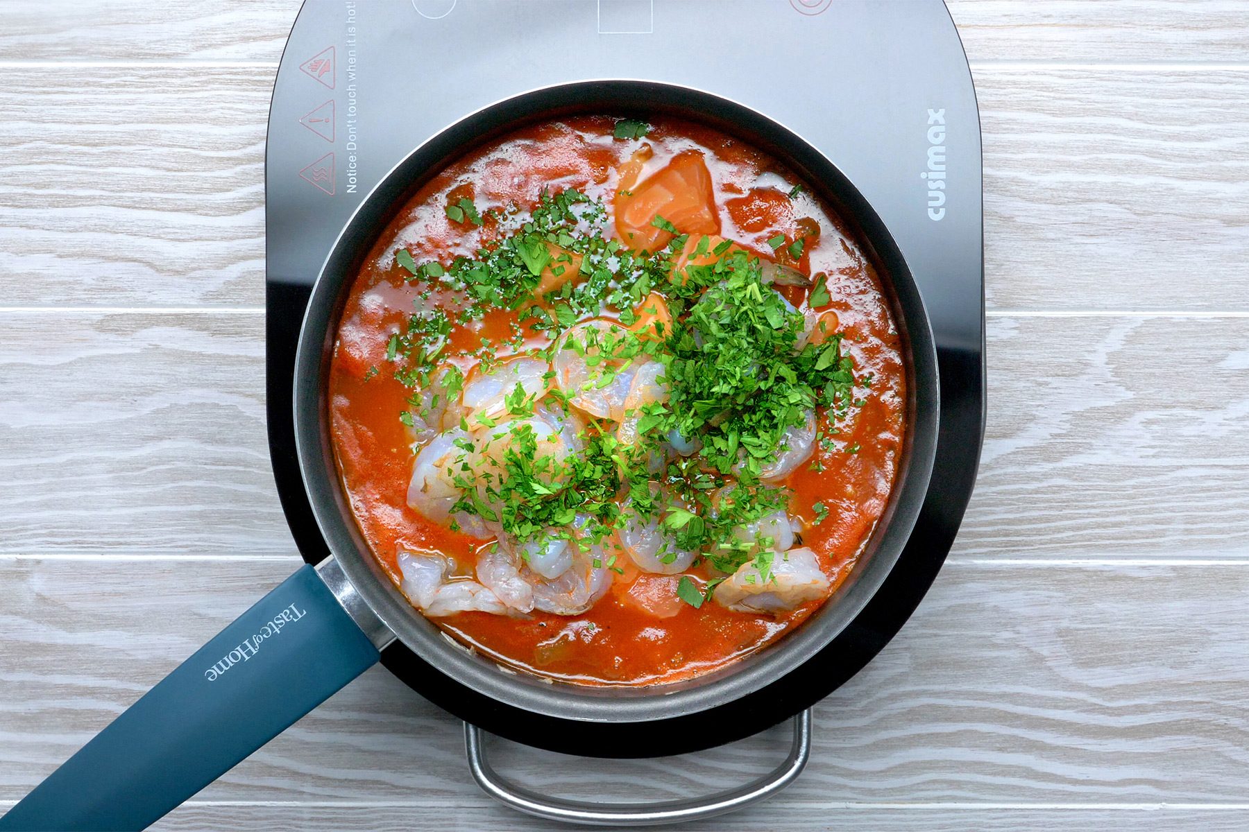 Overhead shot of the same saucepan; stir in salmon; shrimp and parsley; cook 7-10 minutes longer or until fish flakes easily with a fork and shrimp turn pink; discard bay leaf; induction; wooden background;