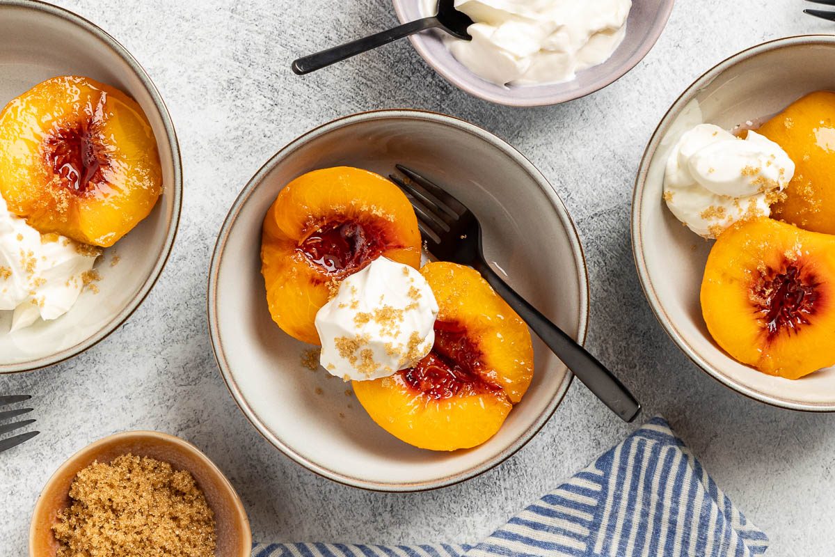 Taste of Home Spiced Peaches recipe photo of the poached peaches served into bowls with dollops of sour cream and sprinkle of bronw sugar.