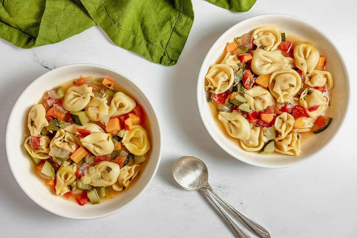 Taste of Home vegetarian tortellini soup in white ceramic bowls next to a green linen napkin.