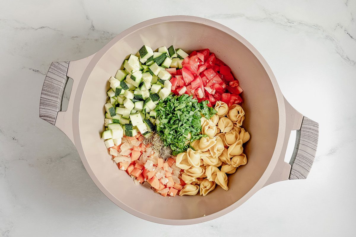Ingredients for Taste of Home vegetarian tortellini soup in a Dutch oven on a marble surface.