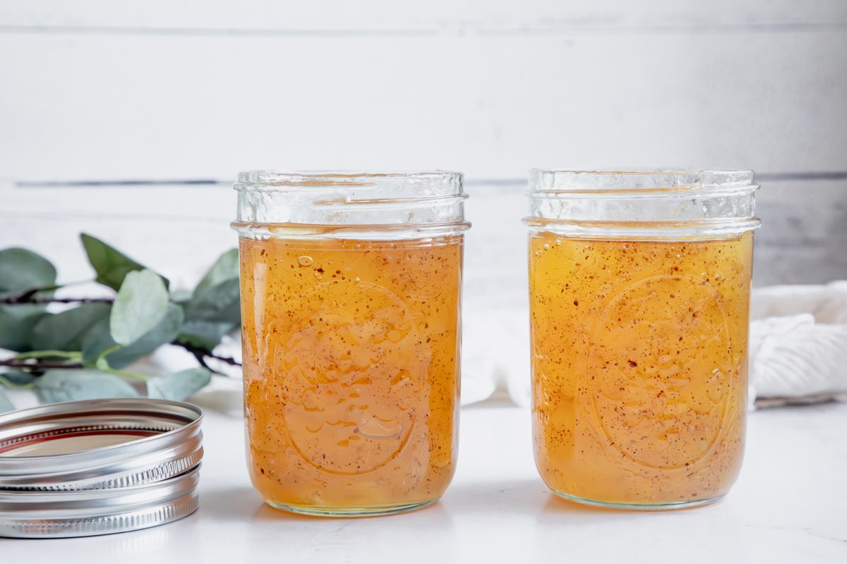Cooked apple jam for Taste of Home in mason jars on a marble surface with lids next to them.