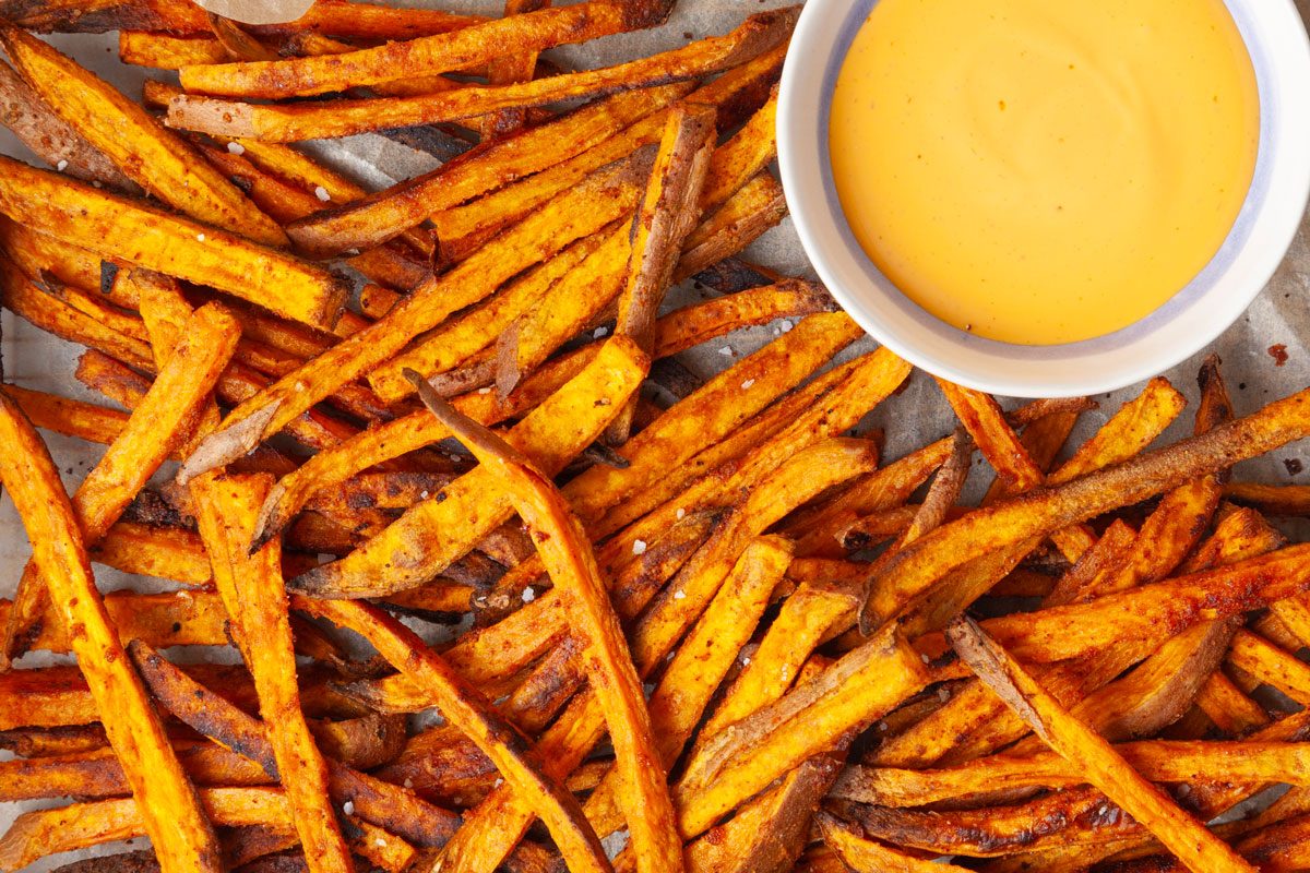 Full yield of Taste of Home Baked Sweet Potato Fries in a copper wire basket lined with parchment, bowl or spicy mayo