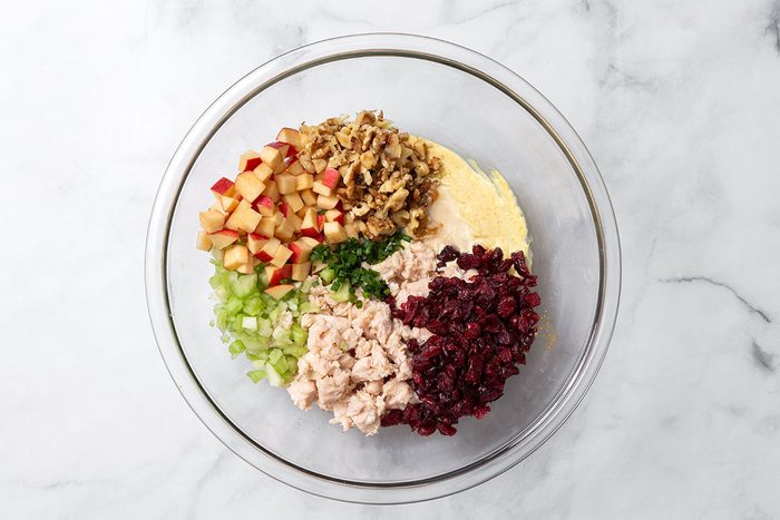 Mayonnaise sauce with chopped apple, onion, celery, walnuts, dried cranberries, and chicken in a mixing bowl