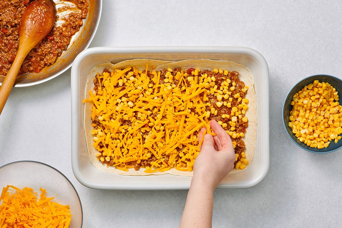 Layering the meat mixture cheese and corn in a baking dish