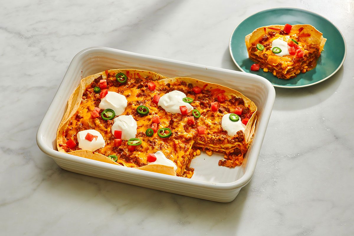 Cooked enchilada casserole with a portion removed and toppings on top