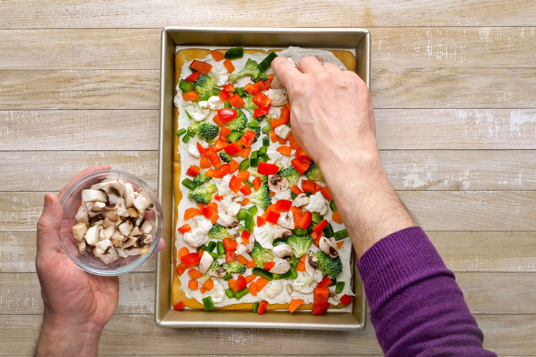 Chopped vegetables being sprinkled over baked pizza.