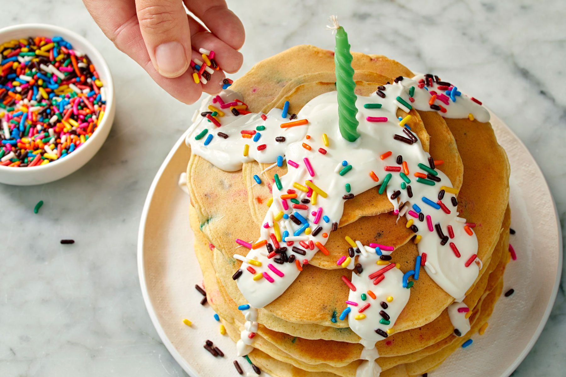 Stack of pancakes being decorated with frosting and sprinkles.