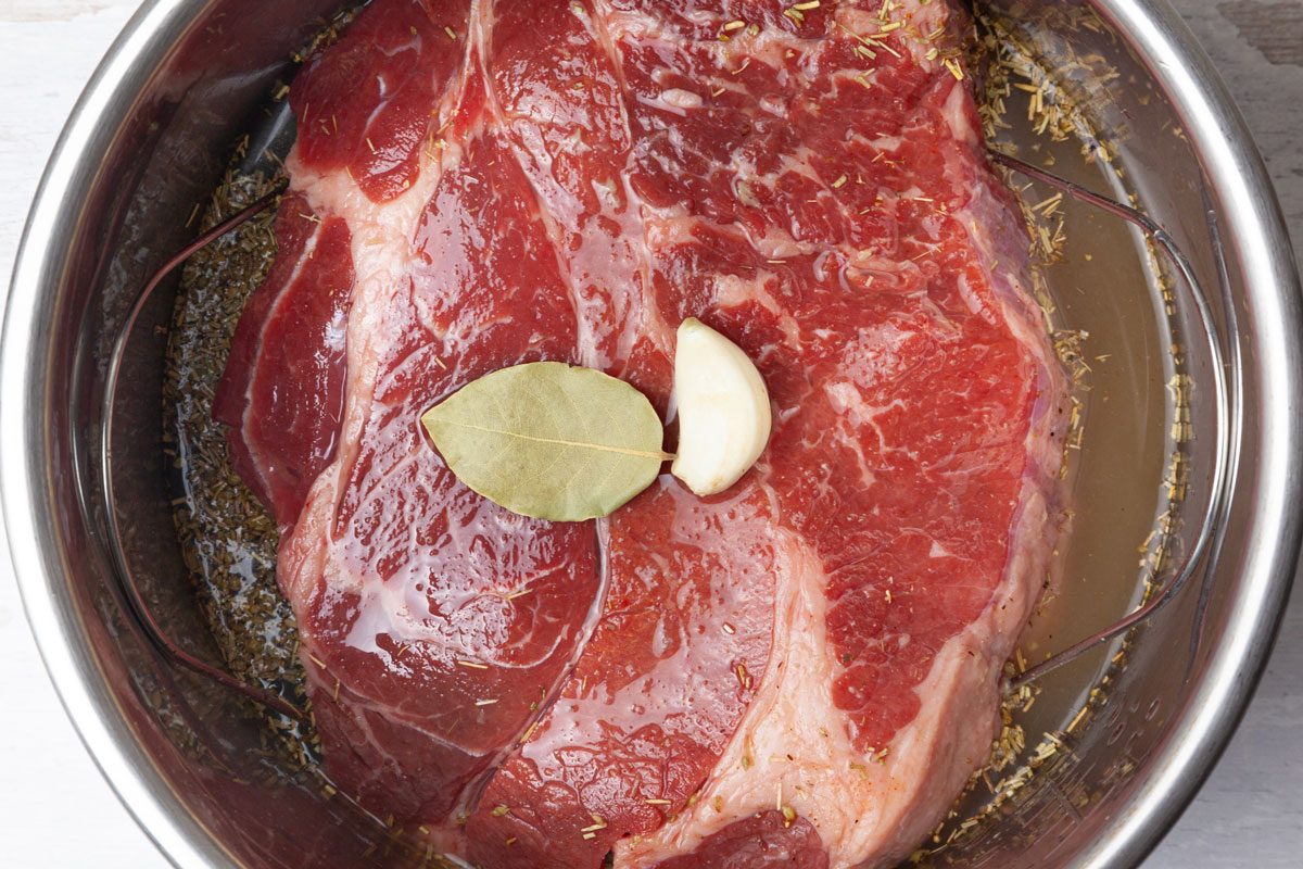 Step 2 of Taste of Home Instant Pot French Dip is to pour the beef broth into the Instant Pot around the roast. Add the bay leaf and peeled garlic clove to the liquid.