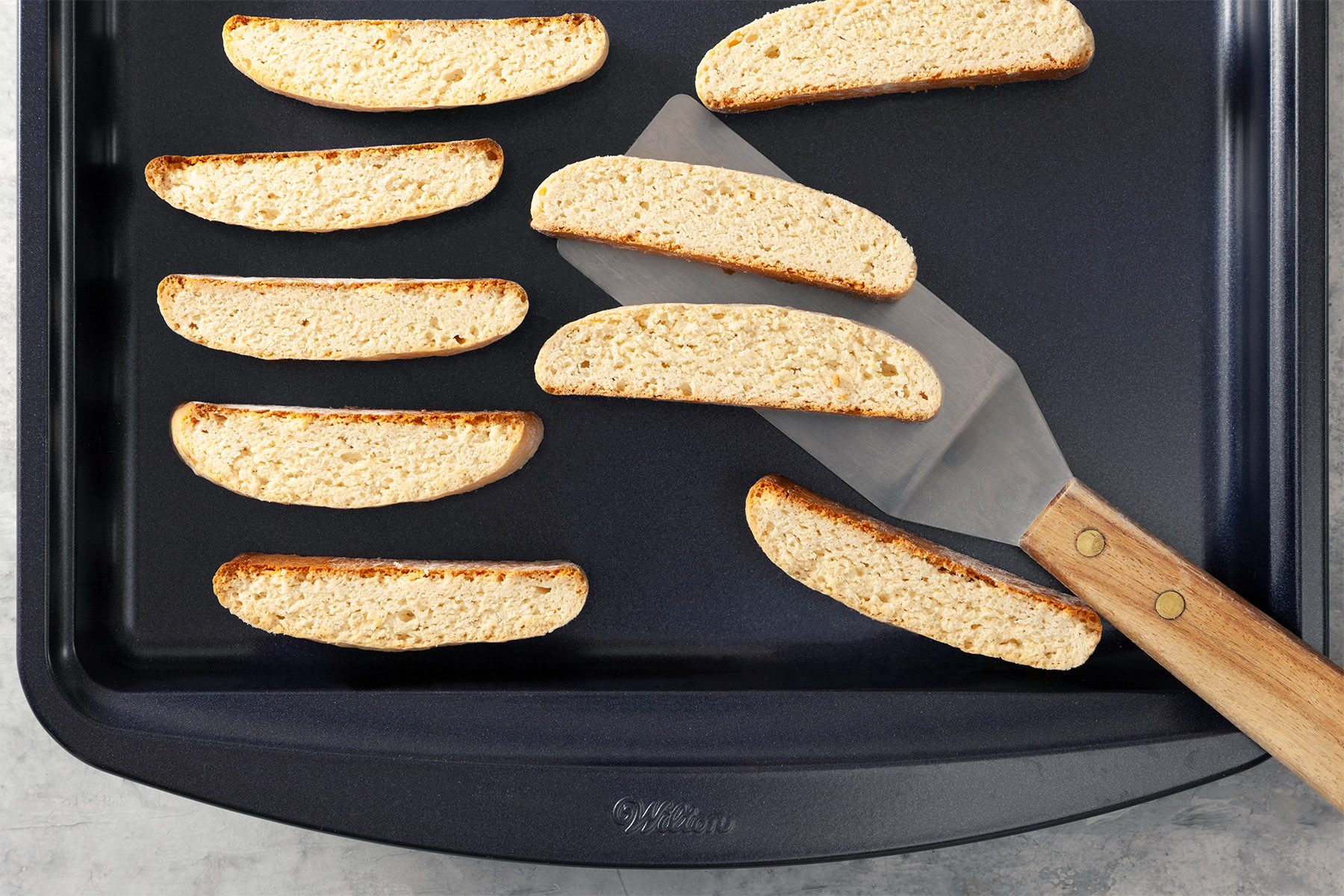 Overhead shot of place cut side down on ungreased baking sheets; bake 5 minutes; turn and bake until firm and golden brown; flat spatula; grey marble surface;