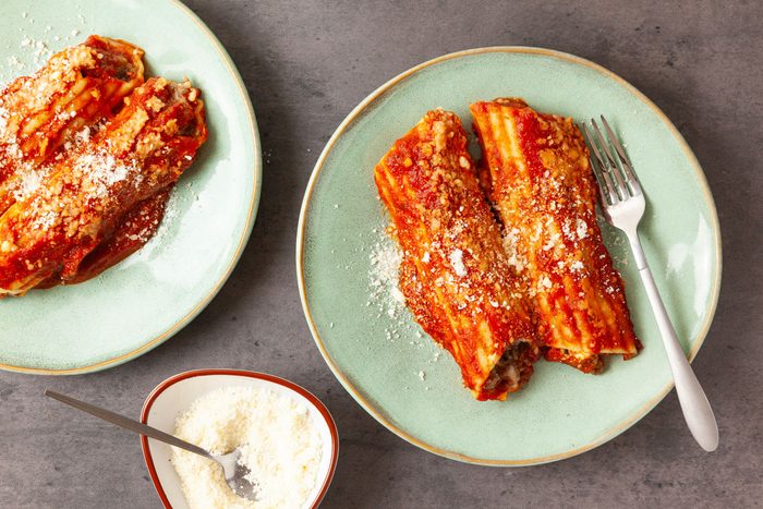 Two servings of Taste of Home Meaty Manicotti on an aqua plate, small bowl of parmesan cheese