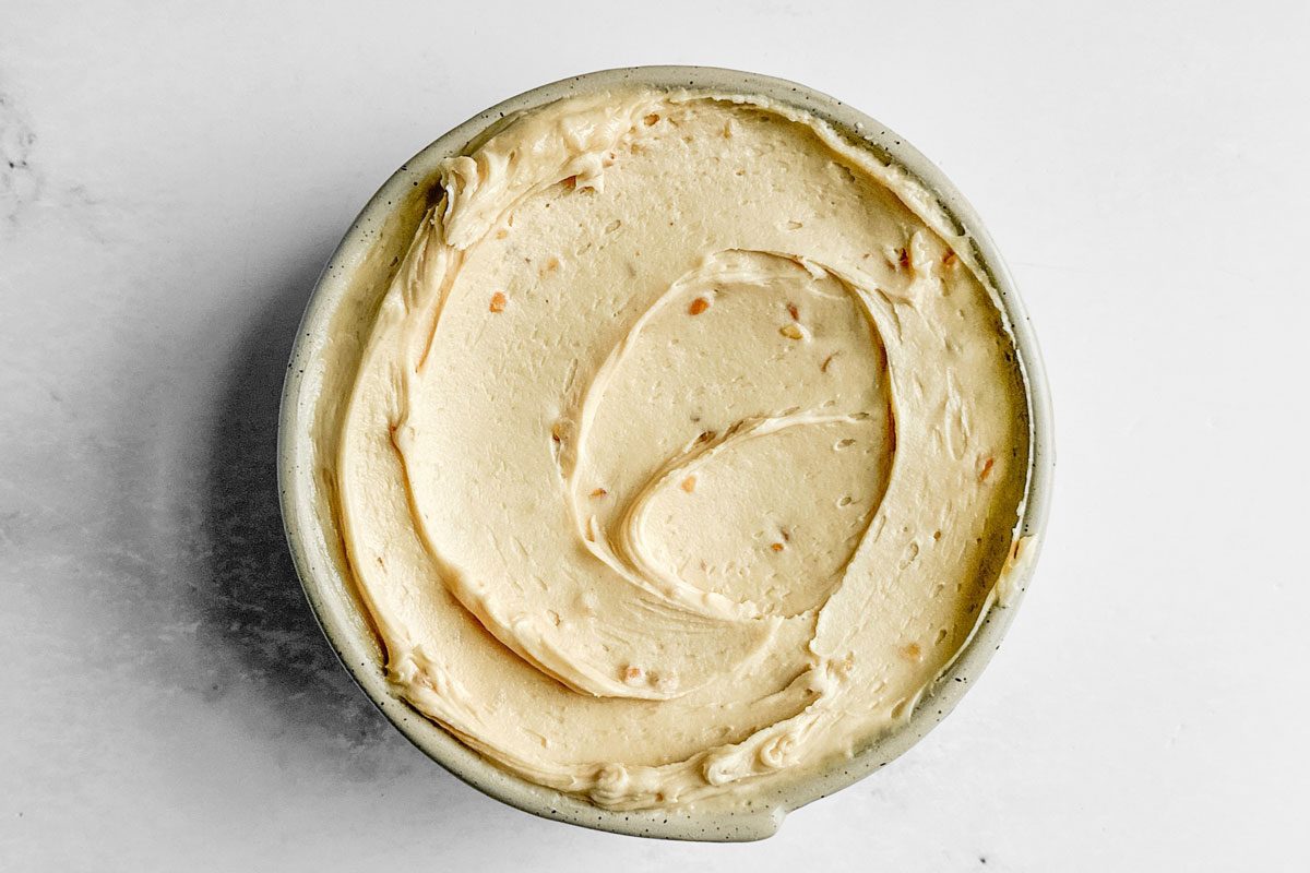Frosting for Taste of Home Peanut Butter Cake in a ceramic bowl on a marble surface
