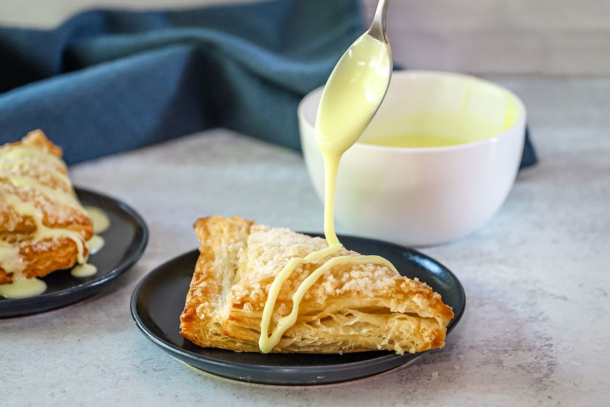 Drizzling thinned powdered sugar icing over an apple turnover.
