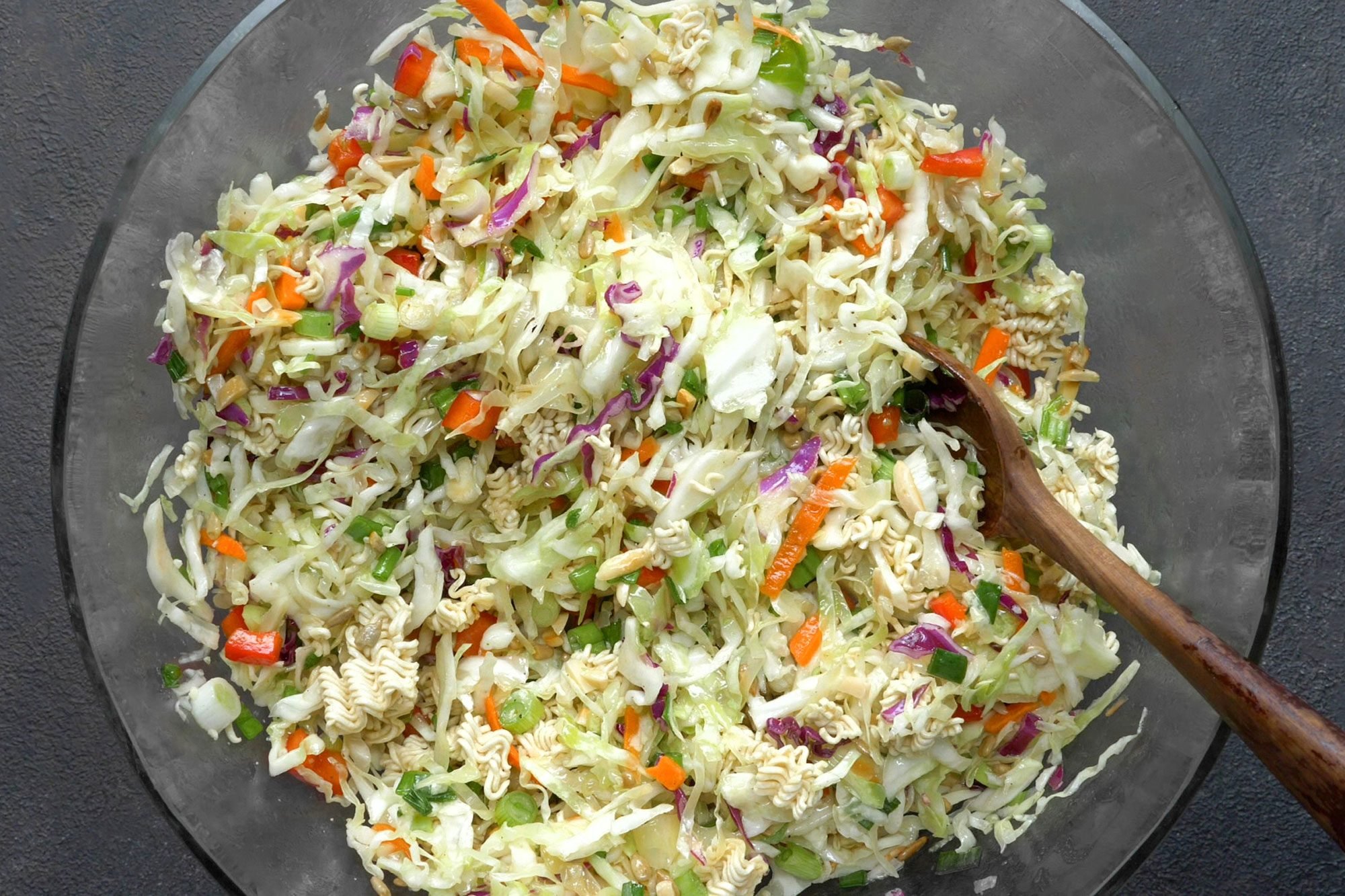 overhead shot; dark grey textured background; stir in noodles, almonds and sunflower kernels with wooden spoon