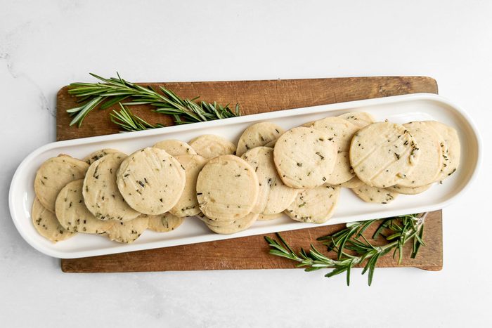 Taste of Home Rosemary Shortbread Cookies on a white tray on a wooden board with sprigs of rosemary