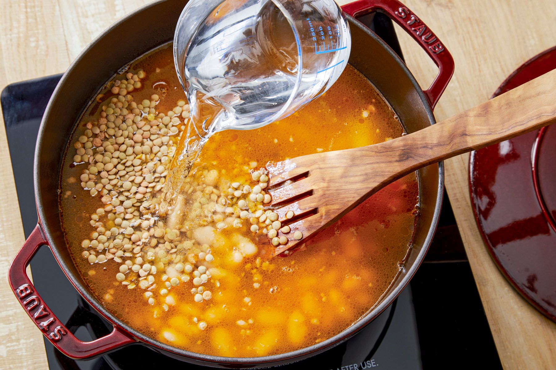 overhead shot; wooden background; Stiring with wooden spatula in lentils beans broth, pouring water in the pan