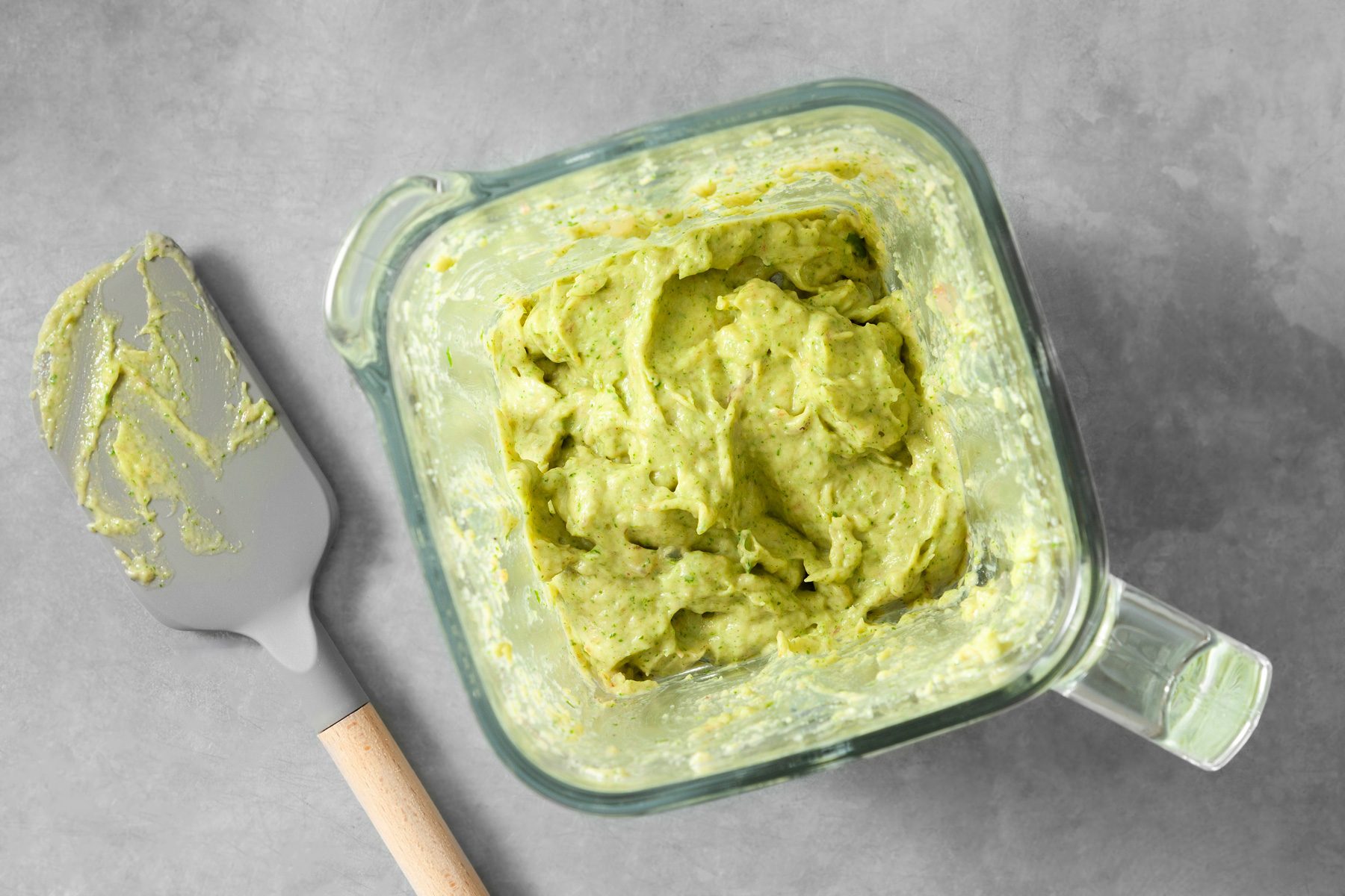 overhead shot; light grey background; ingredients blended utill smooth in the blender; a spatula is lying next to the blender