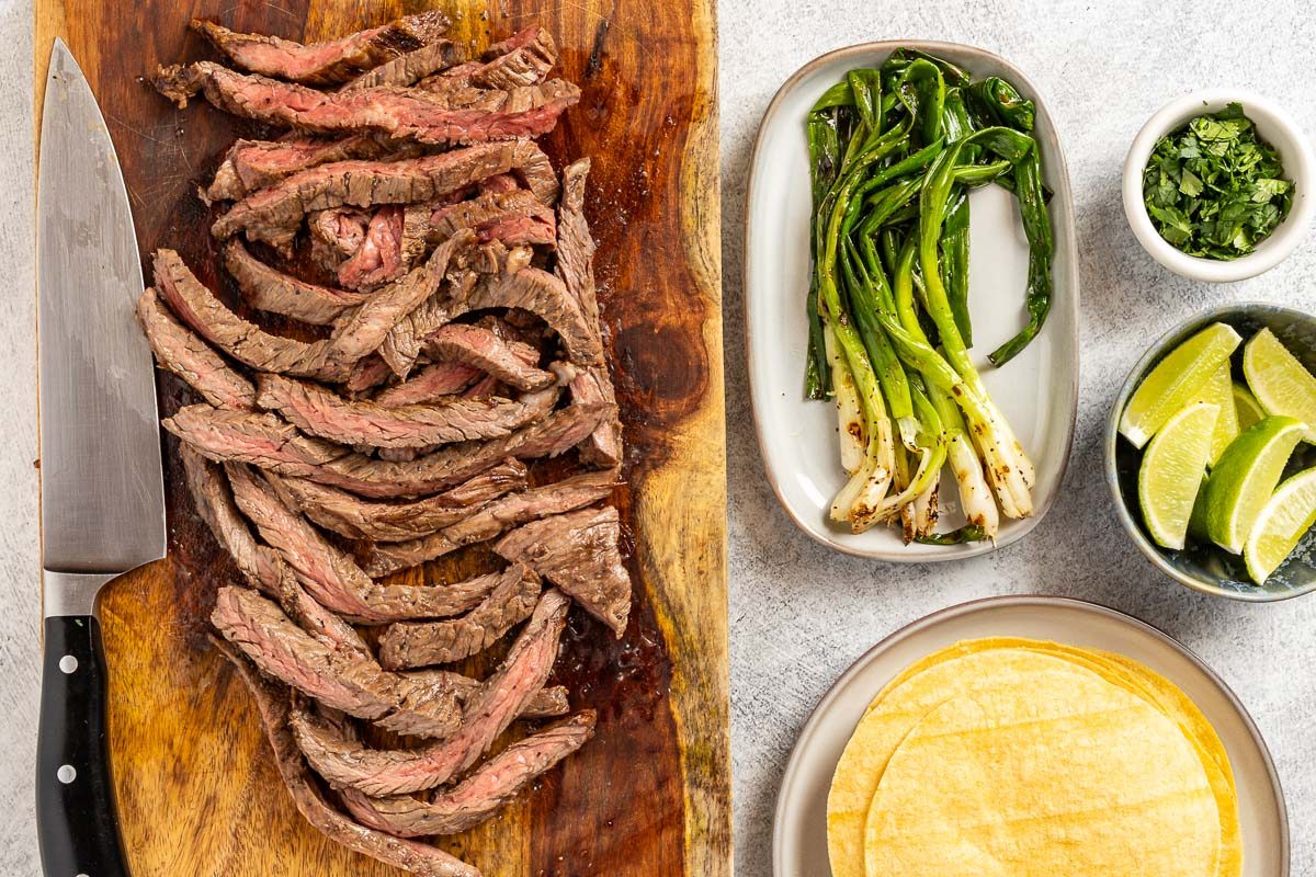 Taste of Home Skirt Steak Tacos recipe photo of the cooked steak, onions, cilantro, lime wedges and tortillas.