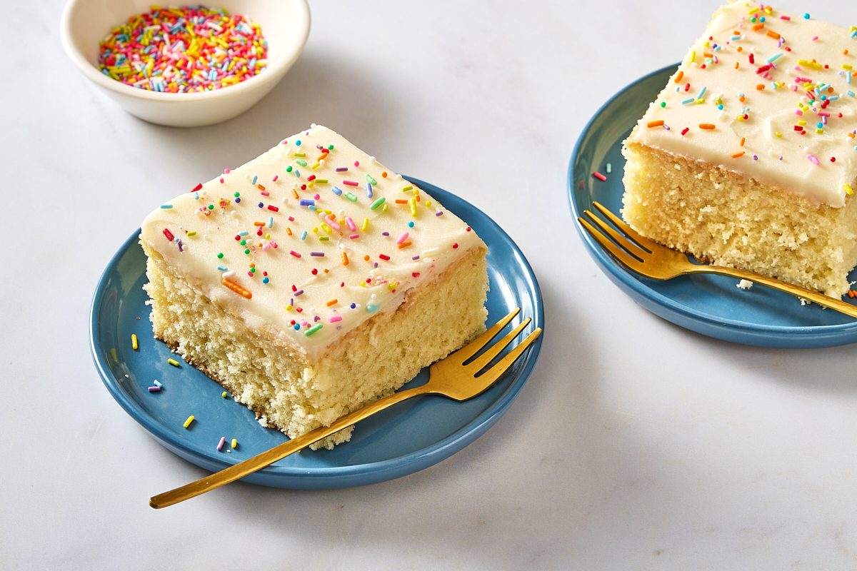 Angled shot of two slices of sugar cookie cake on plates with forks and extra sprinkles