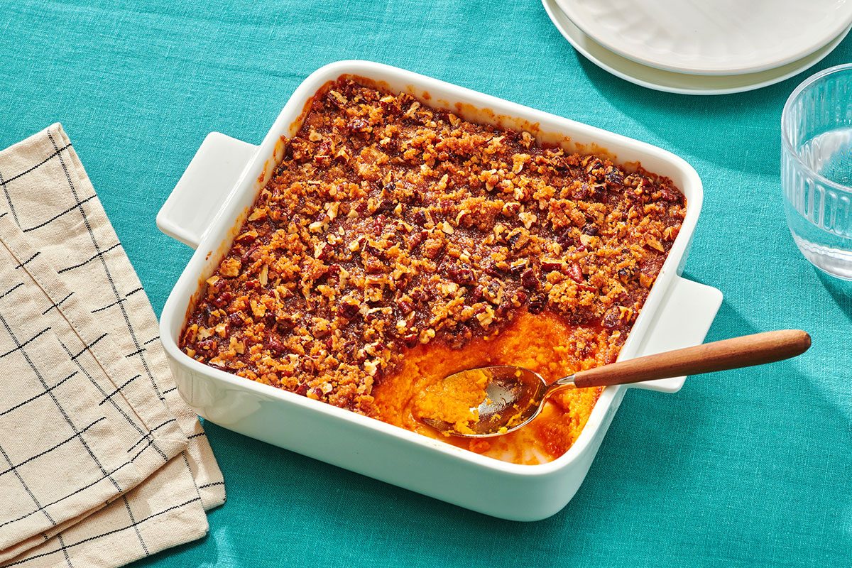 Sweet potato souffle with pecans in a baking dish with a portion removed and a serving spoon in the dish