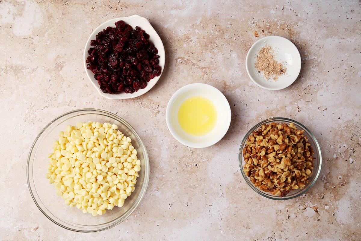 Ingredients for Taste of Home's White Chocolate Bark in small dishes on a beige marble countertop.