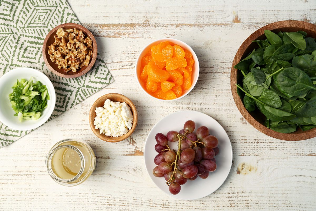 Ingredients for Taste of Home's Spinach Fruit Salad in small dishes on a white wooden board with a green towel.