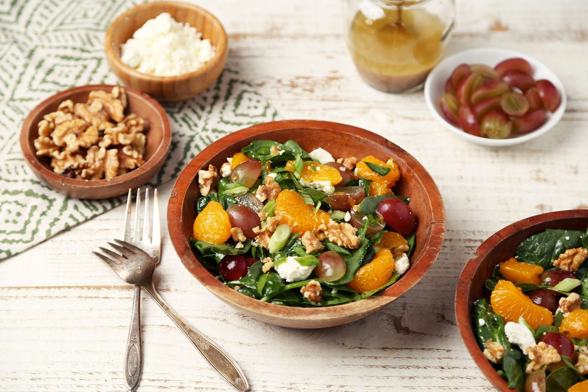 Close up of Taste of Home's Spinach Fruit Salad served in wooden bowls on a white wooden surface with a green towel.