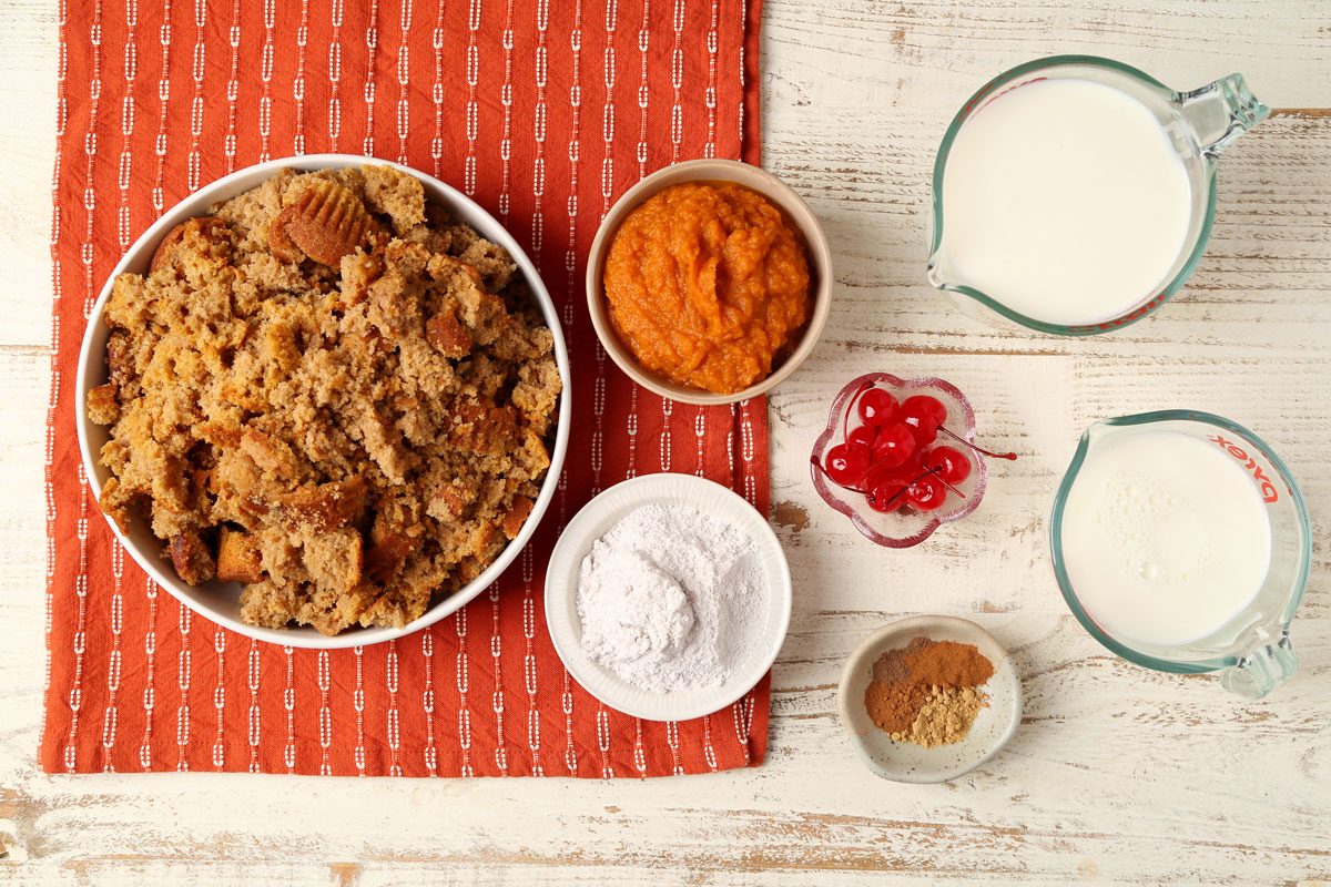 Ingredients for Taste of Home's Pumpkin Trifle laid out in small bowls on a white wooden surface with an orange towel.