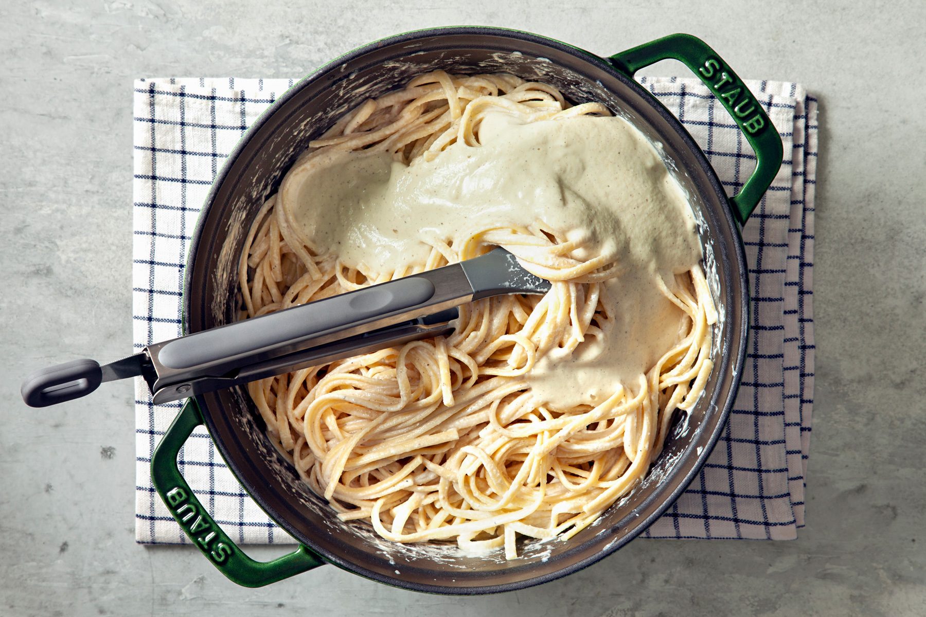 Overhead shot of cook linguine according to package directions; reserve 2 cups pasta water; drain the remaining pasta water; place pasta back in pot; add sauce to pot with pasta; toss to combine;tongs; kitchen towel; grey marble surface