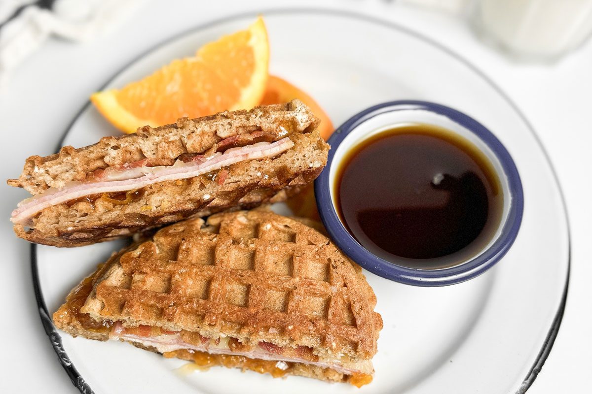 Taste of Home Waffle Sandwich on an enamel plate with orange wedges and maple syrup