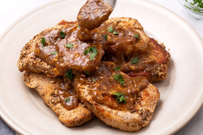 Apple Cider Pork Chops topped with parsley on a serving platter for Taste of Home