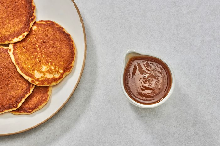 Syrup in a small pitcher with a plate of pancakes nearby