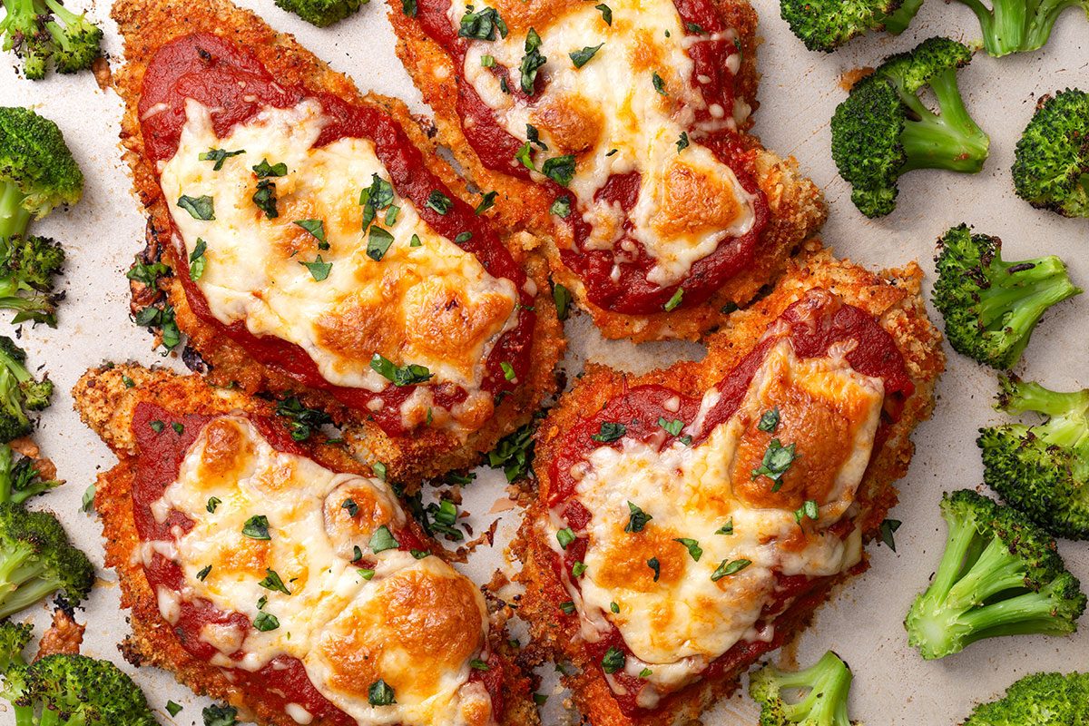 Overhead shot of Baked Chicken Parmesan on a baking pan with roasted broccoli florets