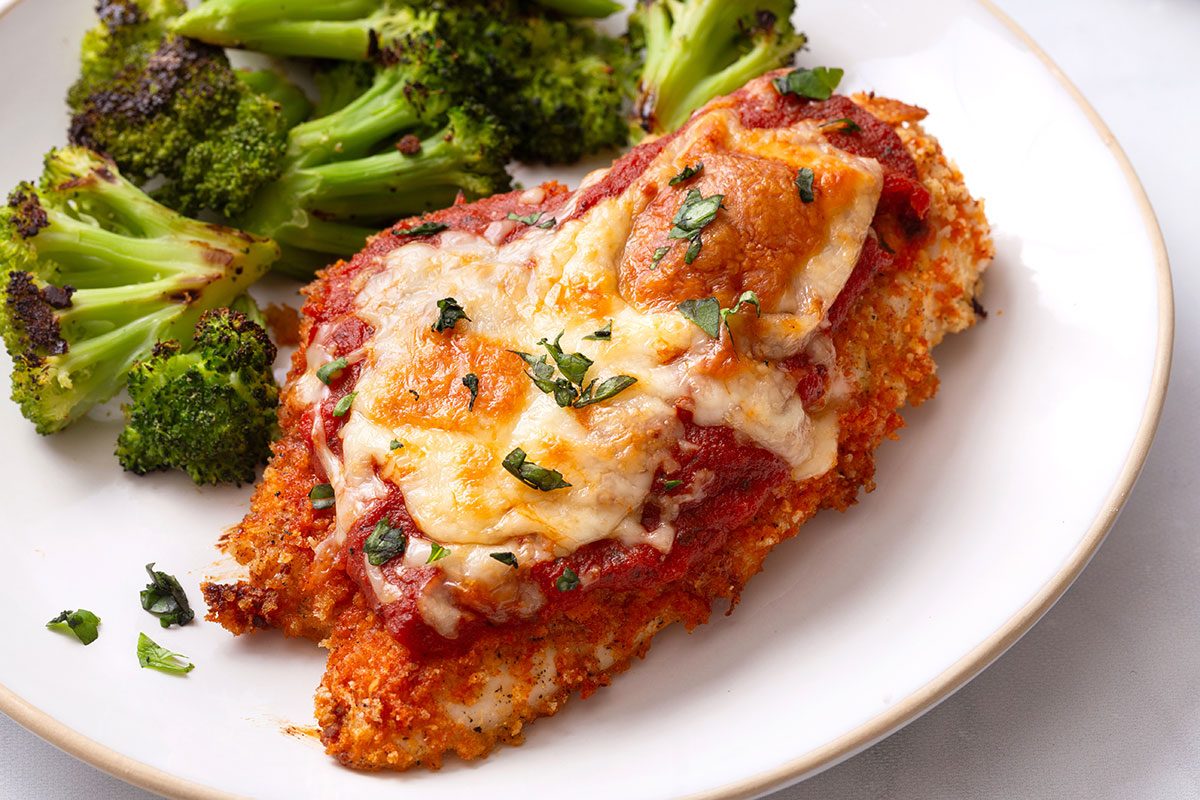 Baked Chicken Parmesan on a plate with a side of roasted broccoli florets for Taste of Home