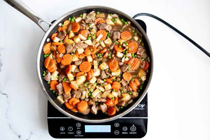 Overhead shot for Taste of Home Beef Potpie with Biscuits, ingredients cooking over an induction cooktop.