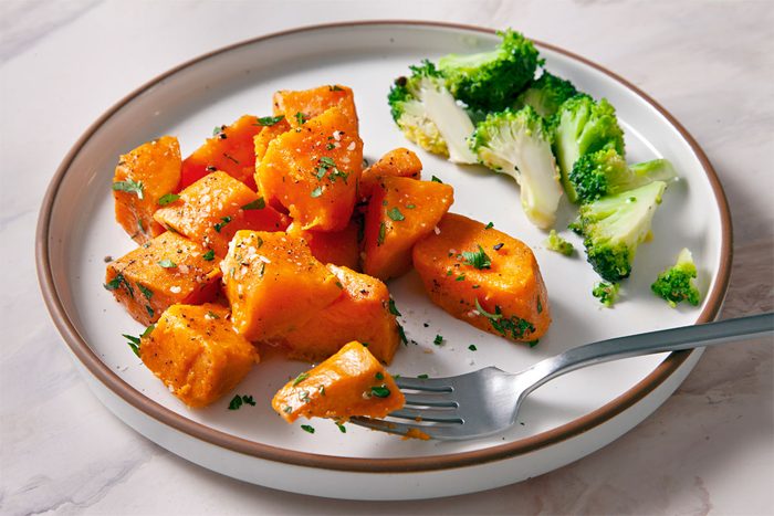 3/4th Shot Of Boiled Sweet Potatoes Garnished With Parsley, Butter And Pepper on a plate with broccoli
