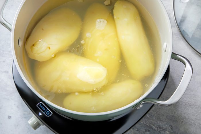A boiling pot on a stove, with steam rising from the water. The heat is visibly reduced, and the lid is off the pot, revealing tender potatoes inside.