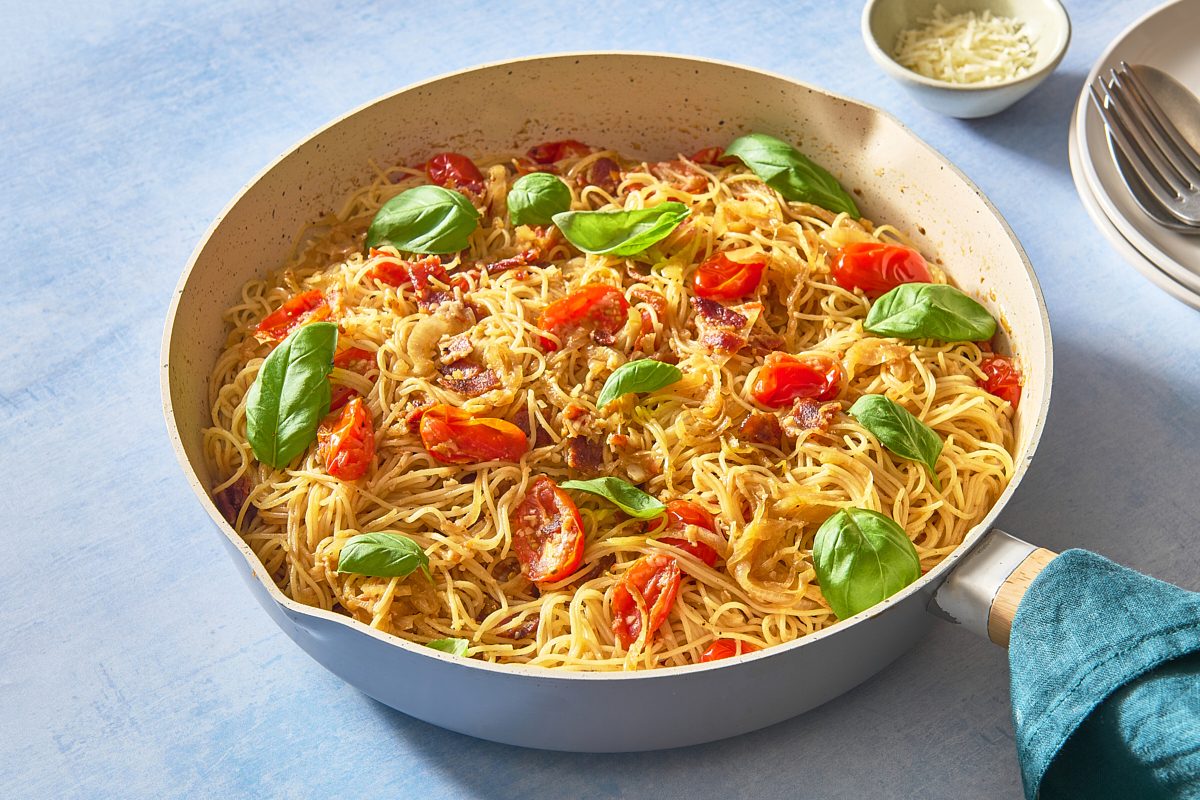 Angled shot of a skillet of caramelised onion pasta topped with fresh basil
