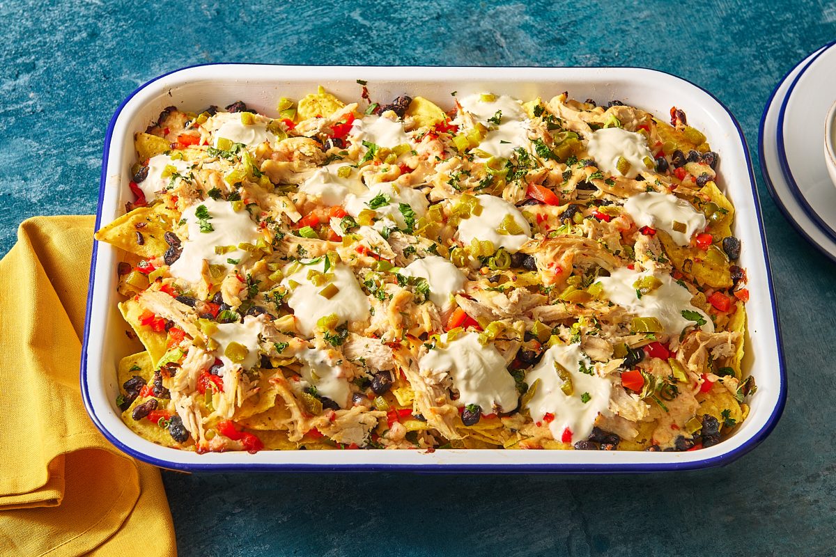 Tray of baked chicken nachos topped with sour cream and jalapeños