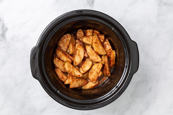 Baked chopped apples and cinnamon seasoning in a slow cooker for step three of Cinnamon Apple recipe for Taste of Home