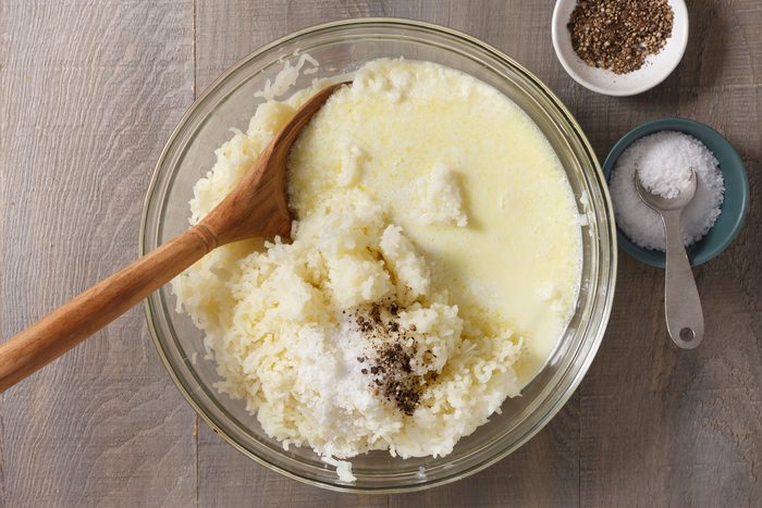 Milk, cream and butter mixture added to mashed potatoes in a large bowl.