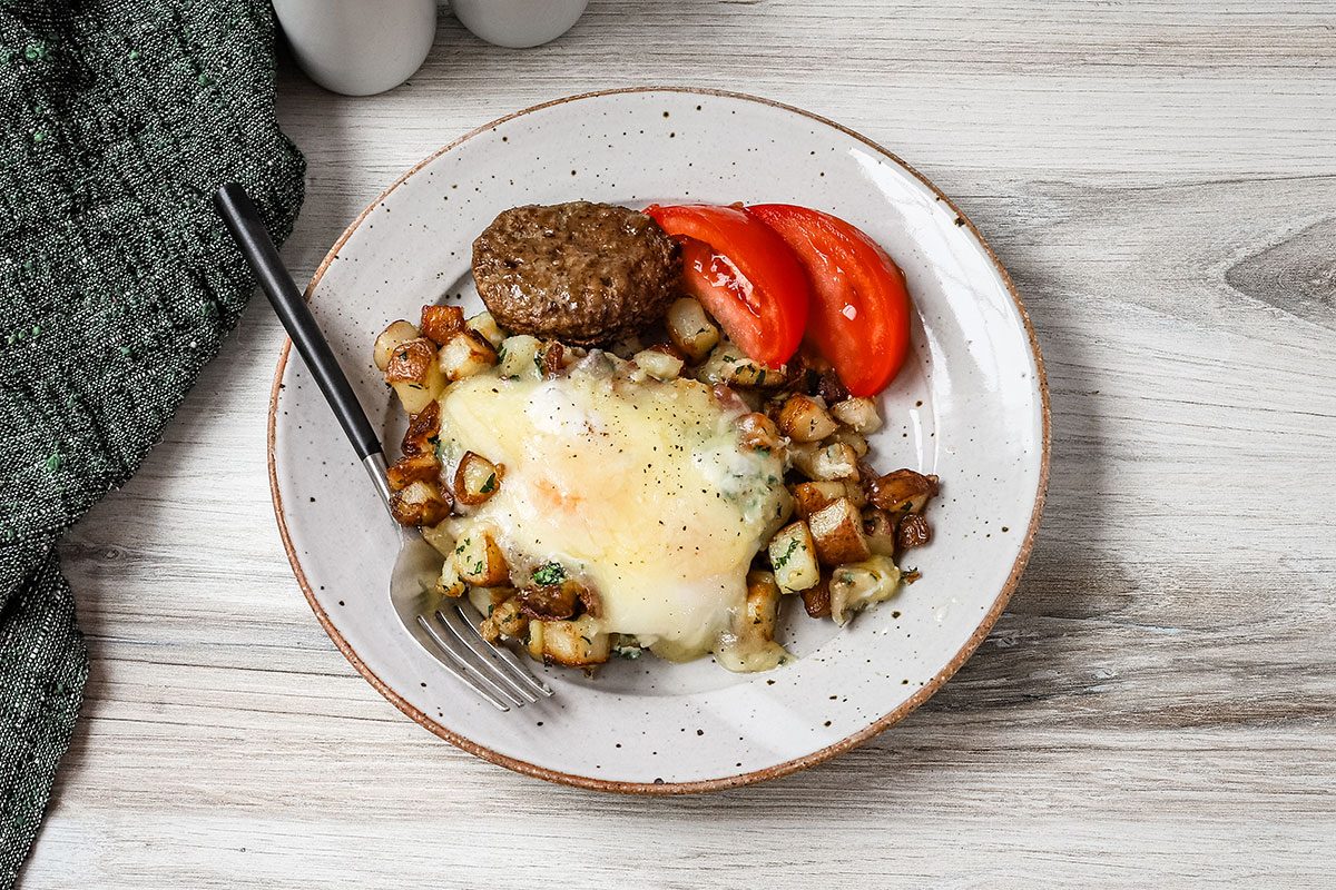 Eggs and potatoes on a plate with tomato wedges and a sausage patty.