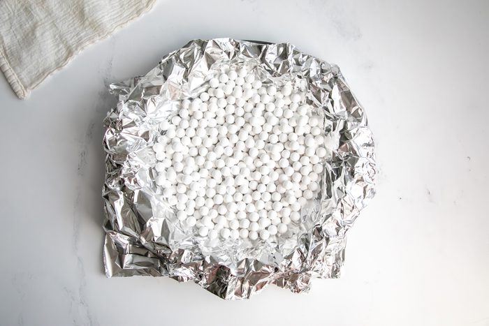 Overhead shot for Taste of Home Fudge Pie, unbaked crust in a pie tin with tin foil and pie beads.