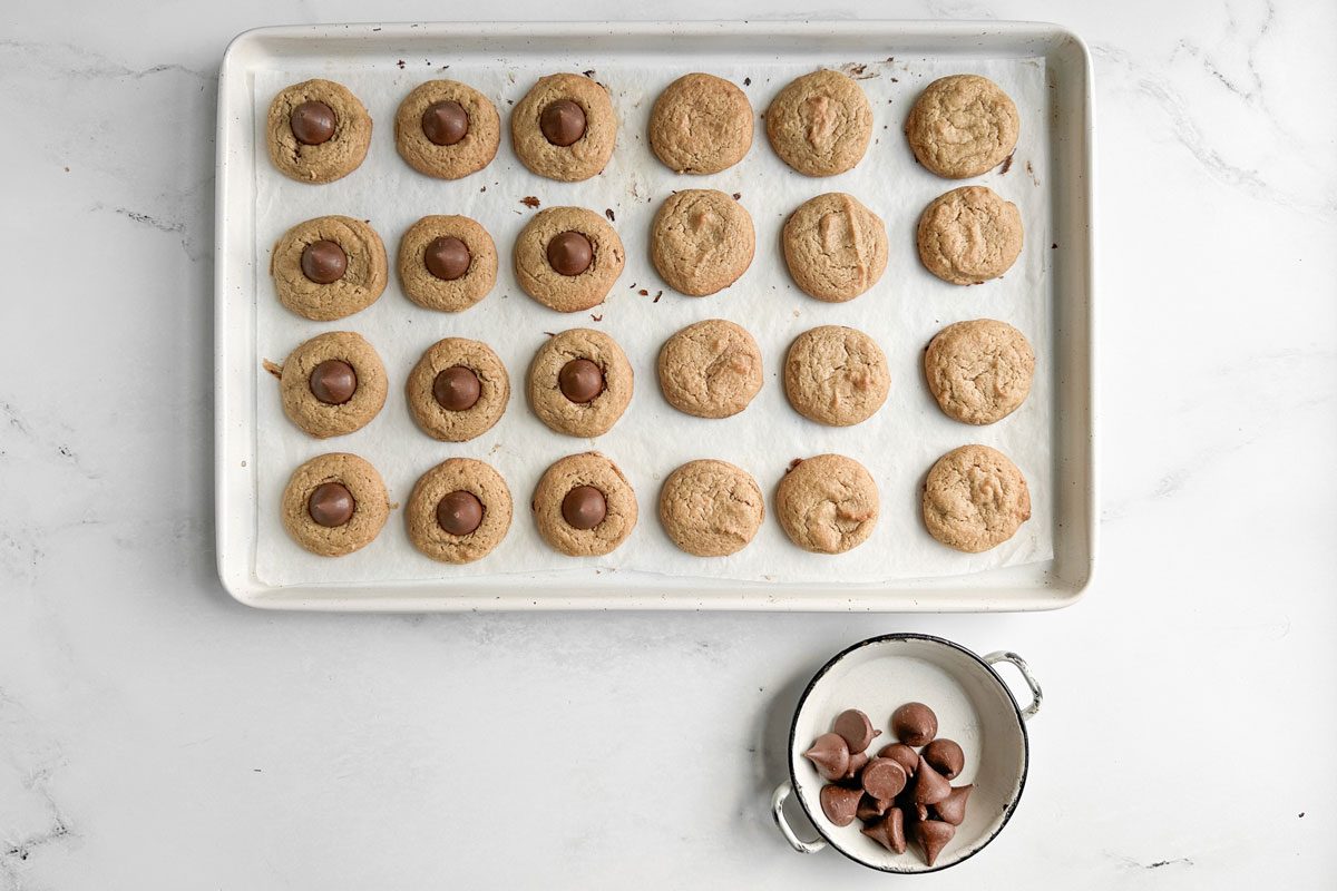 Taste of Home Gluten Free Peanut Butter Blossoms on a white baking sheet next to a dish of chocolate kisses
